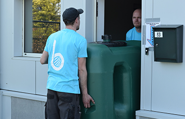 Twee mannen plaatsen een bovengrondse regenwatertank door een deuropening, ideaal voor smalle toegangen.