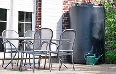 Bovengrondse regenwatertank van kunststof naast een terras voor tuinbesproeiing en wateropslag
