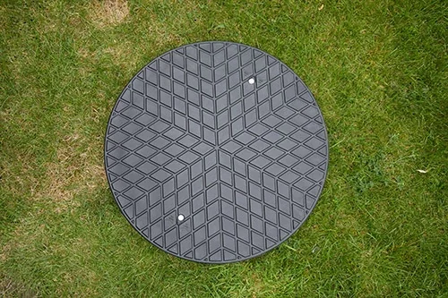 Stappenplan plaatsen van regenwaterput. Rond kunststof deksel van een ingegraven regenwaterput na plaatsing regenwaterput, netjes afgewerkt in een grasveld.